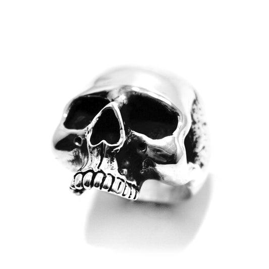 A silver ring featuring a skull design on top, set against a plain background.